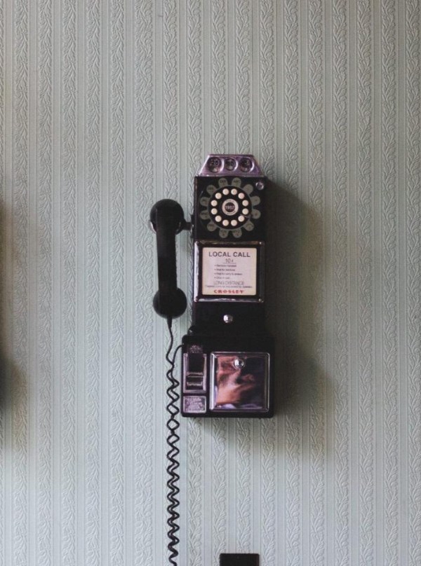 Ein Münztelefon mit Wählscheibe hängt an einer Wand